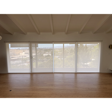Light-filtering shades covering a wide wall of windows in a room with wood flooring and exposed ceil