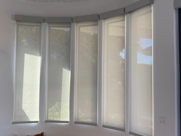 Light-colored roller shades fitted across tall bay windows.