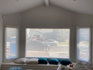 White sheer shades across three windows above a cushioned window seat.