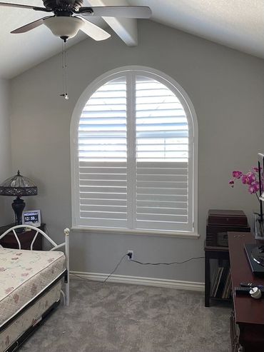 White plantation shutters fitted to an arched bedroom window.