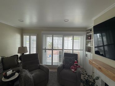 White plantation shutters across living room windows behind two recliners.