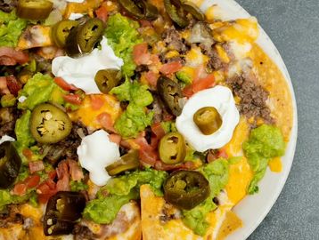 Nachos with beans, ground beef, cheese, sour cream, tomatoes, guacamole, and topped with jalapeños.