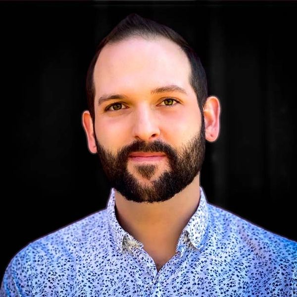 Portrait of a man with a beard and floral shirt against a black background.