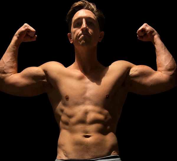 Man flexing muscles under dramatic lighting.