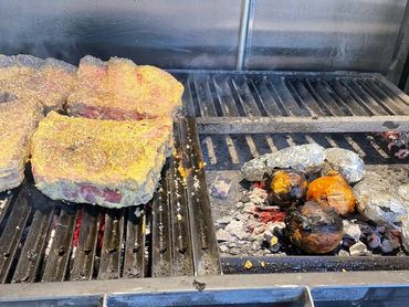 Grilled seasoned steaks and foil-wrapped vegetables cooking on a charcoal grill.