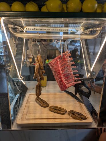 Display case with raw sausages and a rack of ribs on a cutting board.