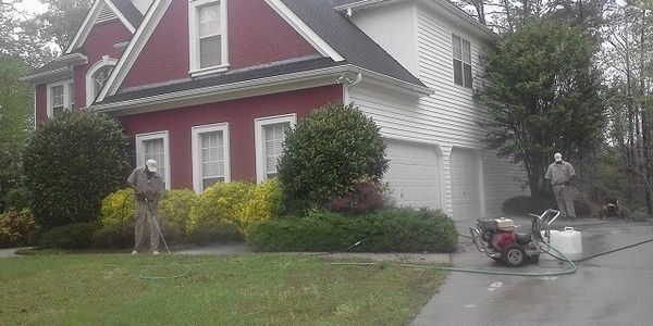 Two workers spraying pesticide on a house lawn and garden.