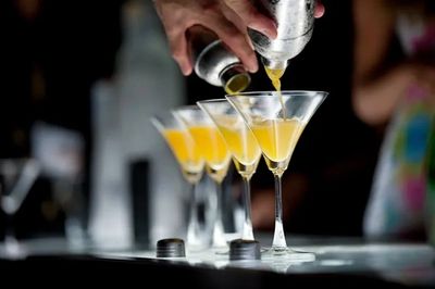 Cocktail pouring into martini glasses in a dim setting.