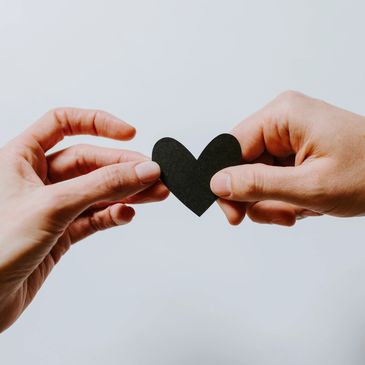 Two hands each holding one side of a paper heart.