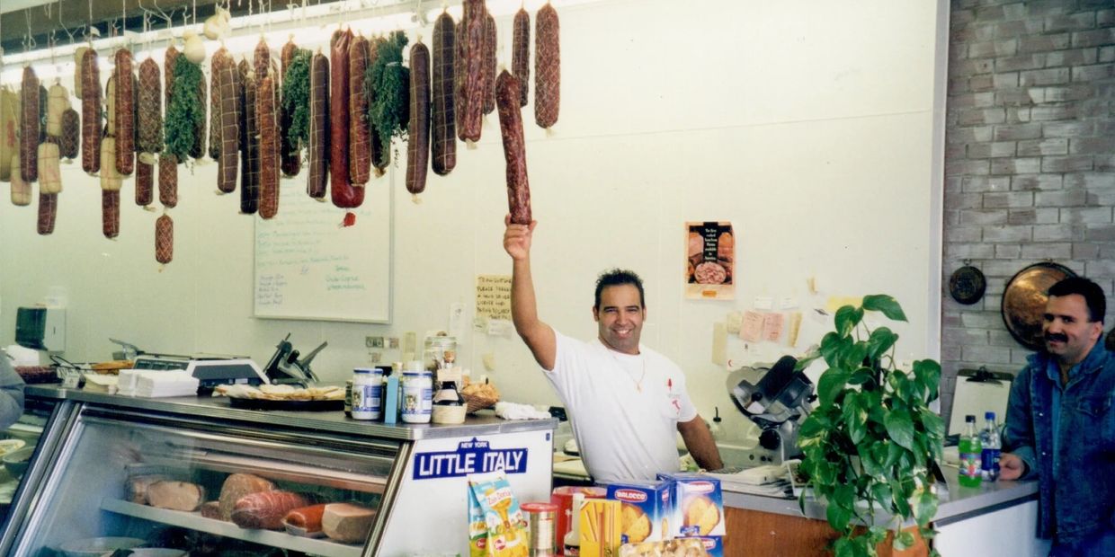 Giacomo holding a handmade salami in his original Italian Market located in Greensboro Nc.