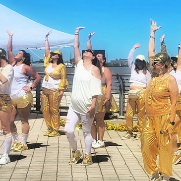 A group of people dressed in gold and white perform a coordinated dance outdoors.