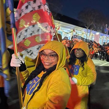 Two women in yellow hoodies holding colorful flags during a nighttime parade.