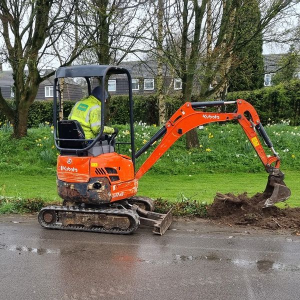 Worker operating a Kubota mini excavator digging soil by the roadside.