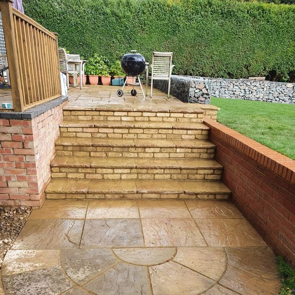 Outdoor brick steps leading to a patio with a grill and chairs.