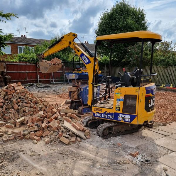 Yellow mini excavator moving bricks on a construction site.