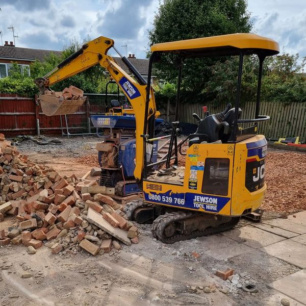 Yellow mini excavator moving bricks at a construction site.