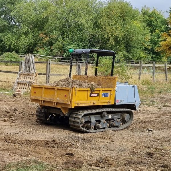 Tracked dumper carrying dirt on a construction site in a rural area.