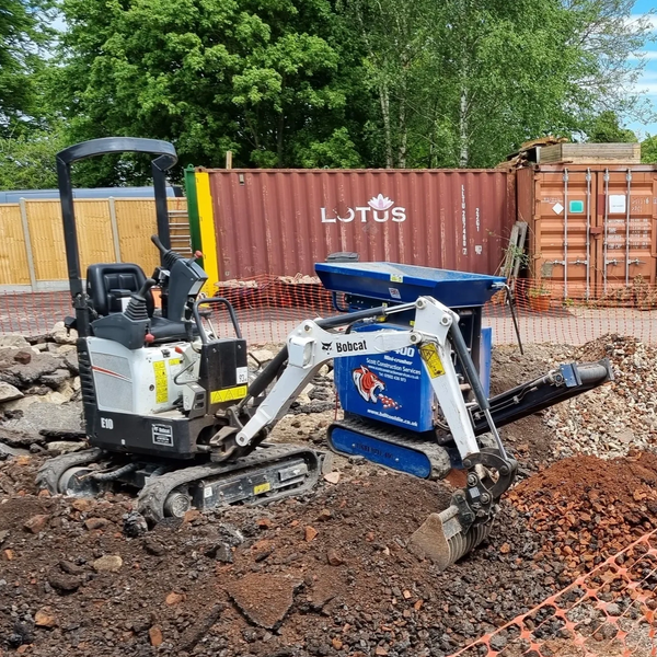 Mini excavator at a construction site with containers and equipment.