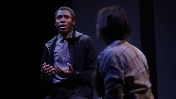 A man and woman look up on a stage lit in blue.