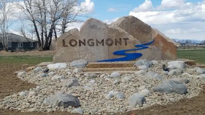 Stone sign with the word Longmont and a blue river design.