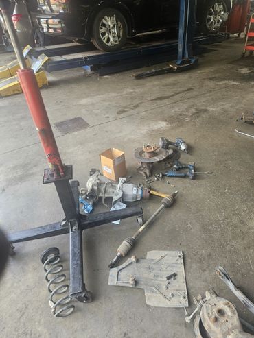 Disassembled car parts and tools on a garage floor near a vehicle lift.