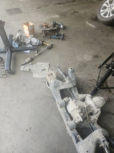 Disassembled car suspension and drivetrain parts on a workshop floor.