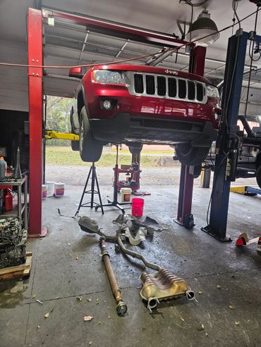 Red Jeep SUV lifted in a garage with removed exhaust parts on the floor.