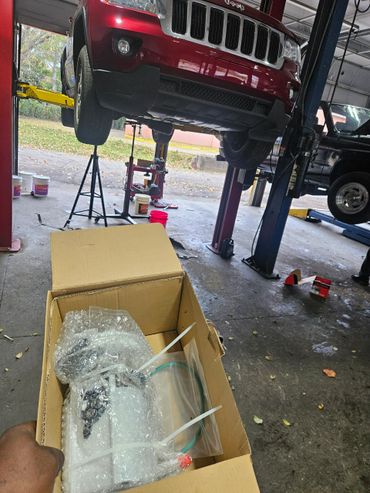 A red Jeep on a lift in a garage with a box of bubble-wrapped parts.
