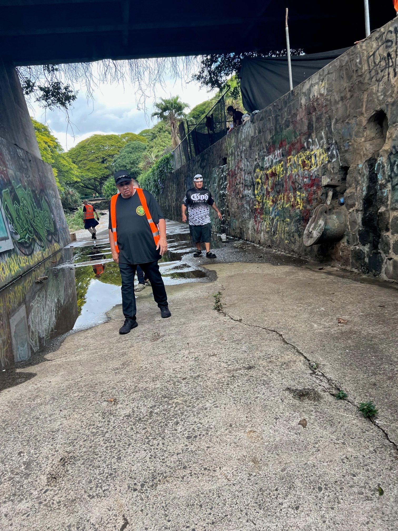 Men walking under a graffiti-covered bridge on a wet pathway.