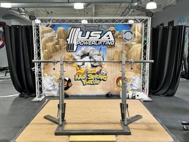 Powerlifting setup with a barbell and USA Powerlifting banner for 2024 AAO Spring Battle.