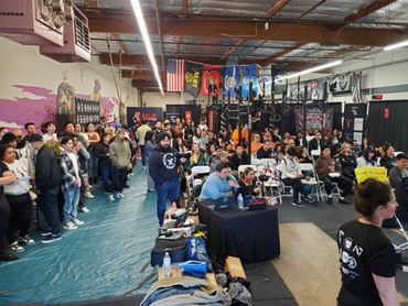 Crowded gym holding a powerlifting event with spectators and announcers.