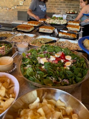 Buffet spread with salads, sandwiches, and chips.