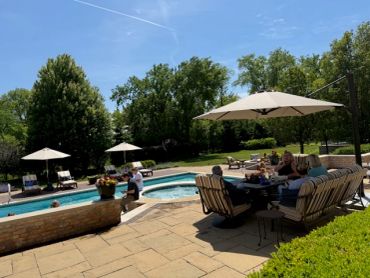 People relaxing by a sunny pool with umbrellas and lounge chairs.