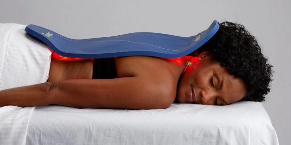 Woman relaxing with a red light therapy device on her back.