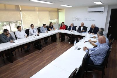 A group of people in a formal meeting around U-shaped tables in a conference room.
