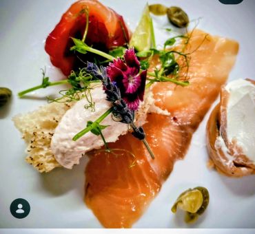 Elegant smoked salmon dish garnished with herbs, edible flowers, and creamy accompaniments.