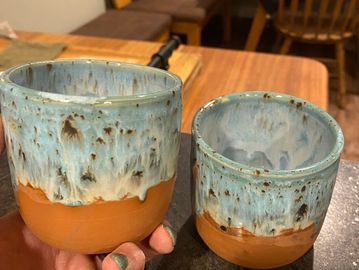 2 ten ounce cups with a lower terra cotta matte glaze with an upper speckled blue dripping glaze.