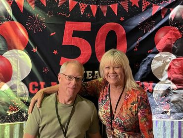 Two people smiling at a 50th celebration with festive decorations.