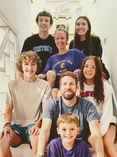 A happy family of eight posing together on stairs, smiling warmly.