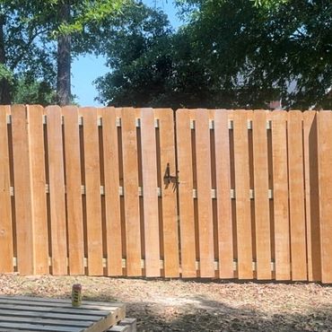 Newly installed wooden fence with a gate in a sunny backyard.