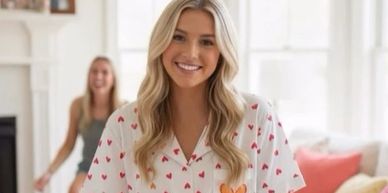 Smiling woman in heart-patterned pajamas sitting on a sofa indoors.