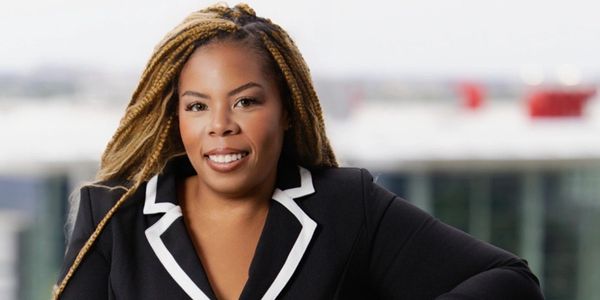Confident woman with braided hair wearing a black blazer with white trim.