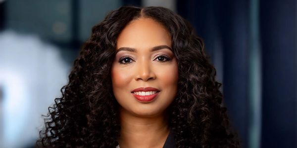 A confident woman with curly hair smiling warmly at the camera.