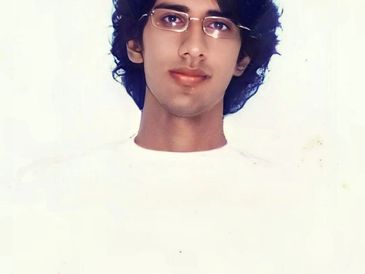 Young man with glasses and curly hair wearing a white shirt.