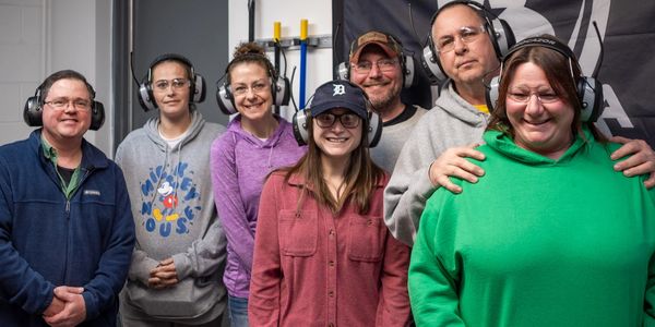 A group of seven people wearing hearing protection and smiling indoors.