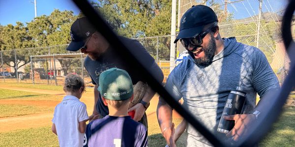 Two men and two boys at a baseball field, exchanging baseball gloves.