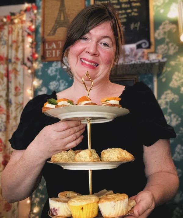 Woman holding a three-tiered tray of pastries and appetizers.