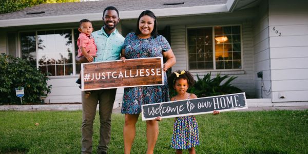 Beautiful family of 4 stands in front of their new home.