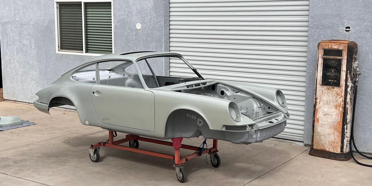 Classic car body shell on a dolly near an old gas pump outside a garage.