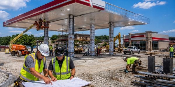 Two construction workers reviewing plans at a gas station under construction.